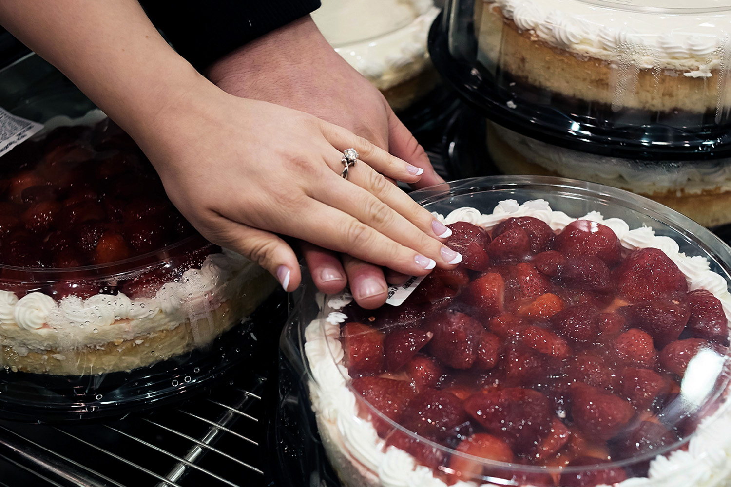 Bride and groom showing off their engagement ring over a strawberry cheesecake at Costco