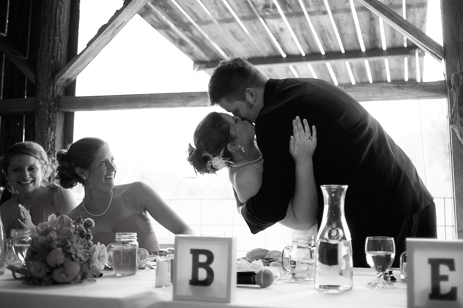 bride and groom kissing after the guest clinked their glasses at the Enchanted Barn wedding reception