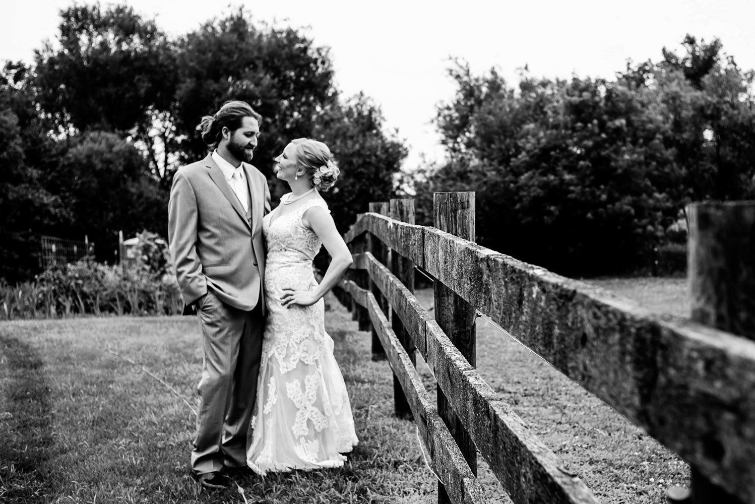 bride and groom standing by a fence before their backyard wedding