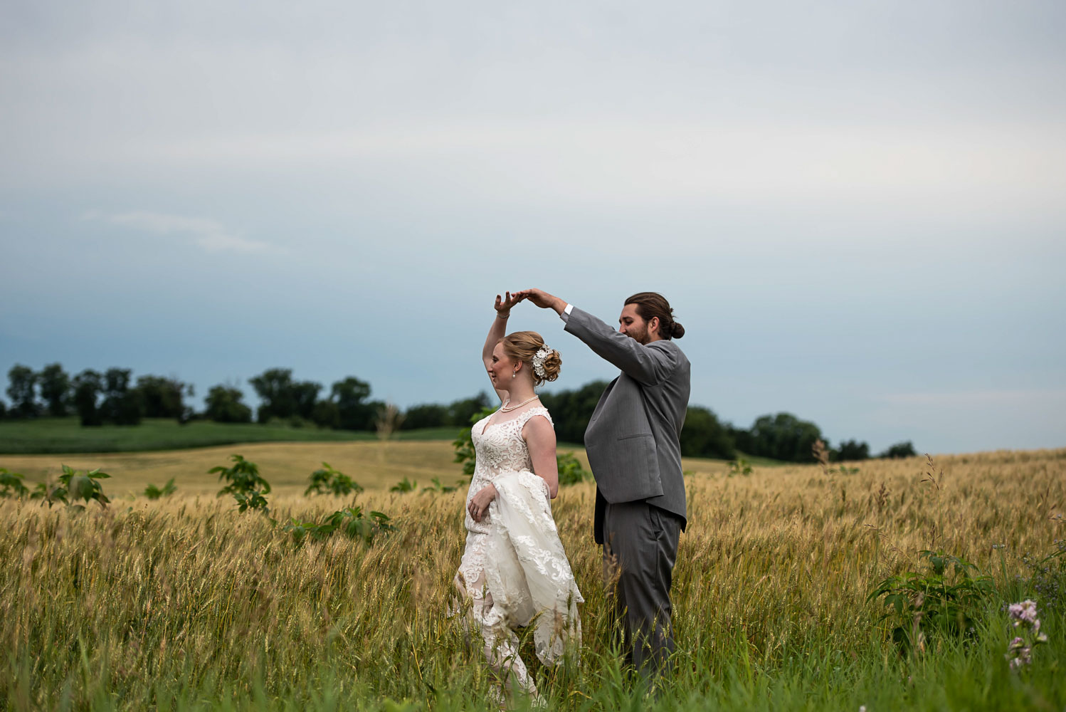 bride and groom dancing in a field of yellow grasses on their summer wedding day