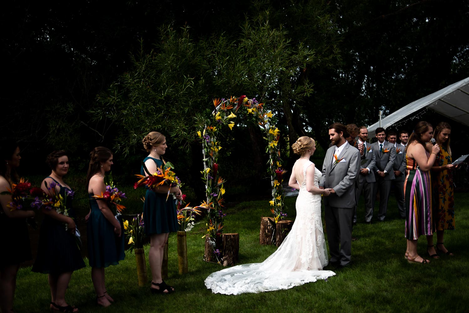bride and groom standing under the arch decorated with tropical flowers during their summer wedding ceremony