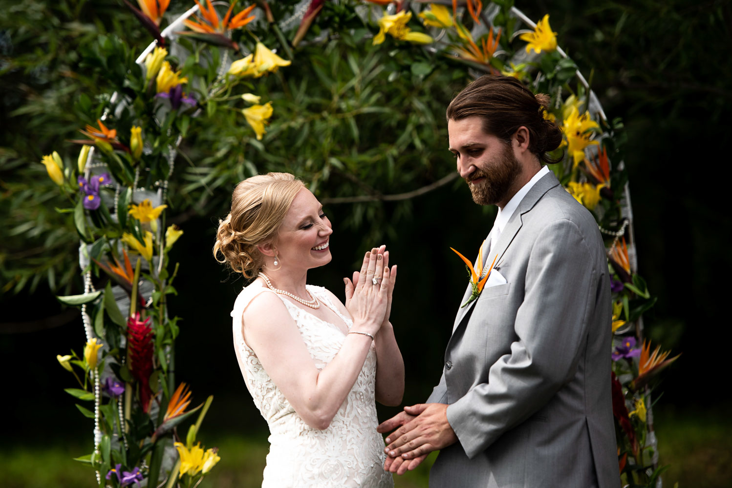 bride and groom standing under an arch decorated with tropical flowers