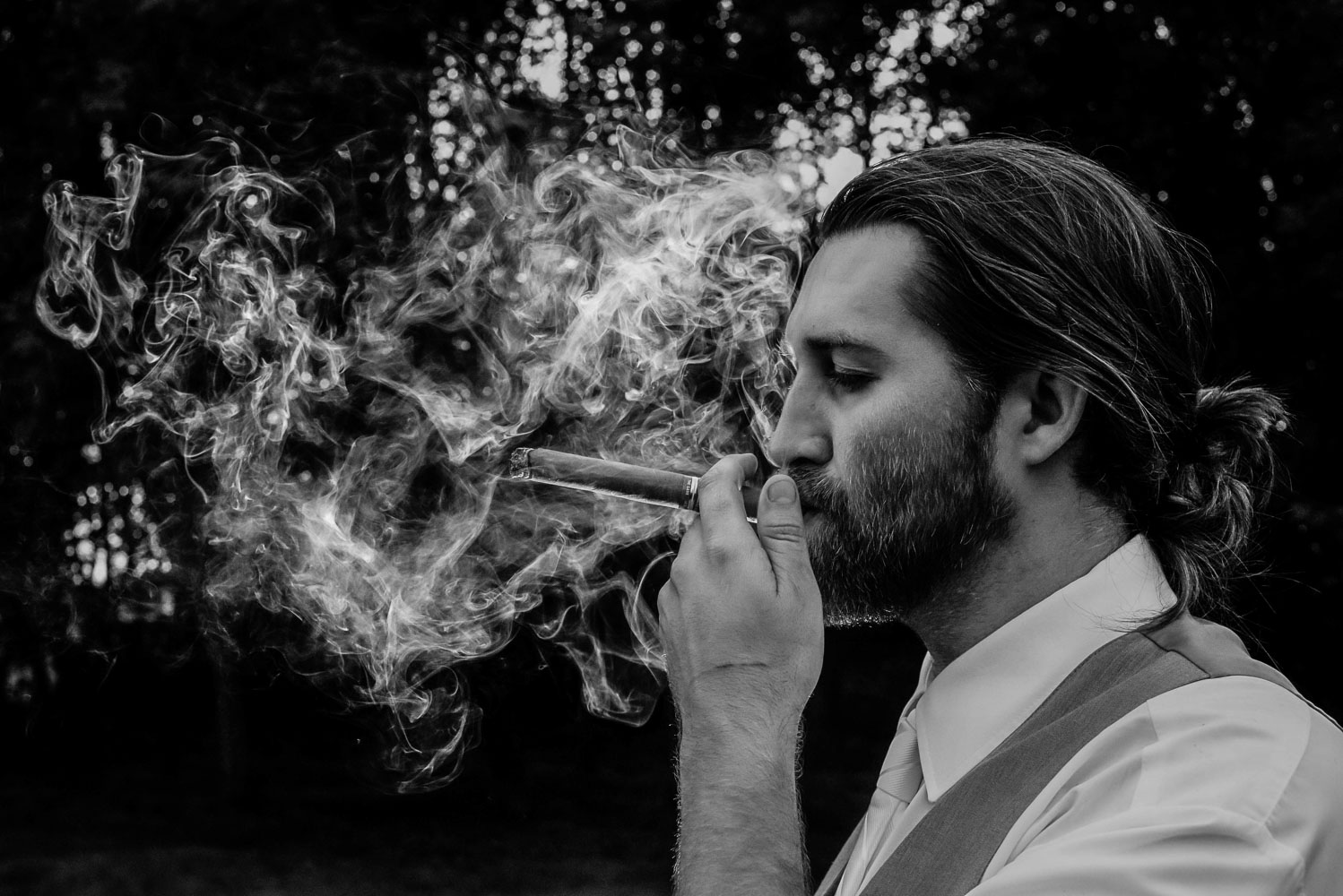 groom smoking a cigar with the smoke backlit during his Minnesota wedding