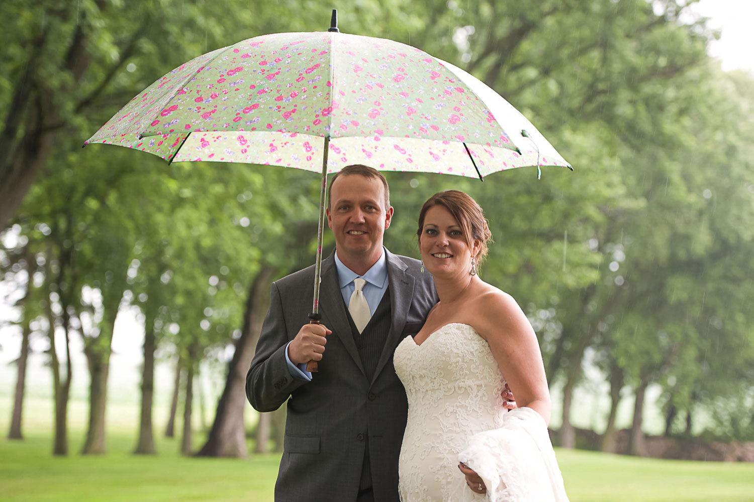 bride and groom holding an umbrella in the rain on their wedding day