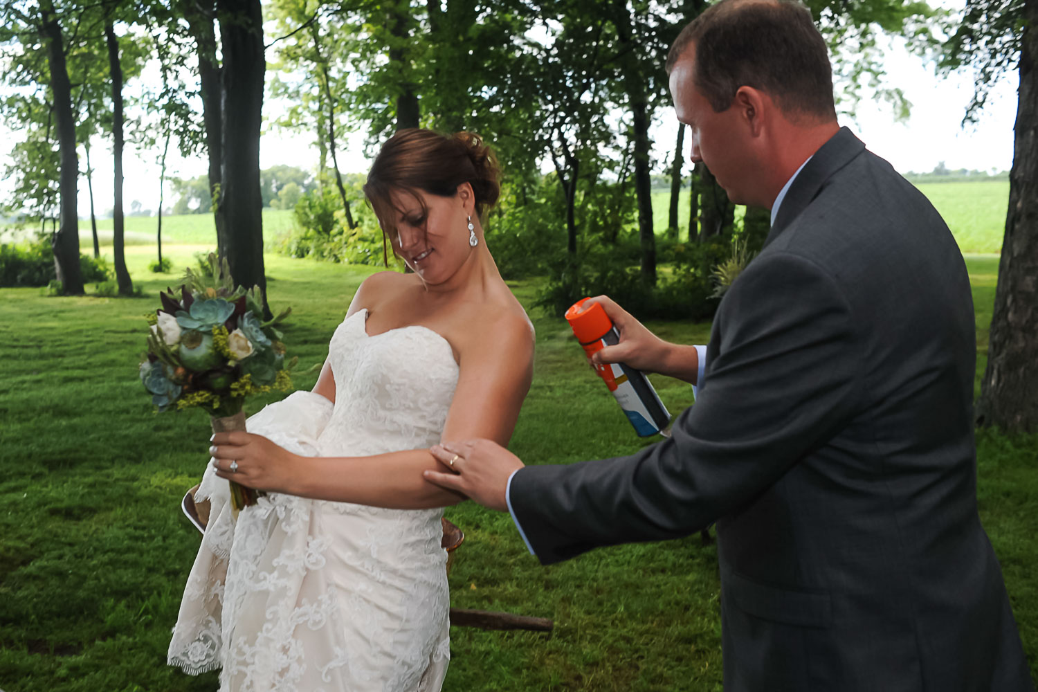 groom spraying mosquito repellant on the bride for their Iowa farm wedding