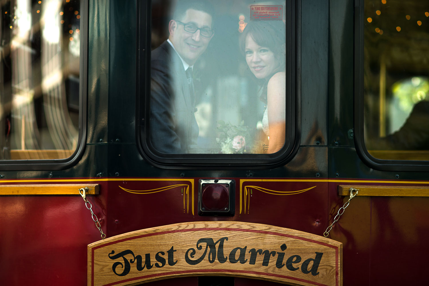 bride and groom looking out the window of a trolley with a just married sign