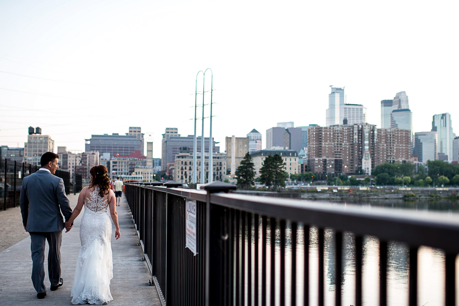 bride and groom walking by the river in Minneapolis with the skyline in the background