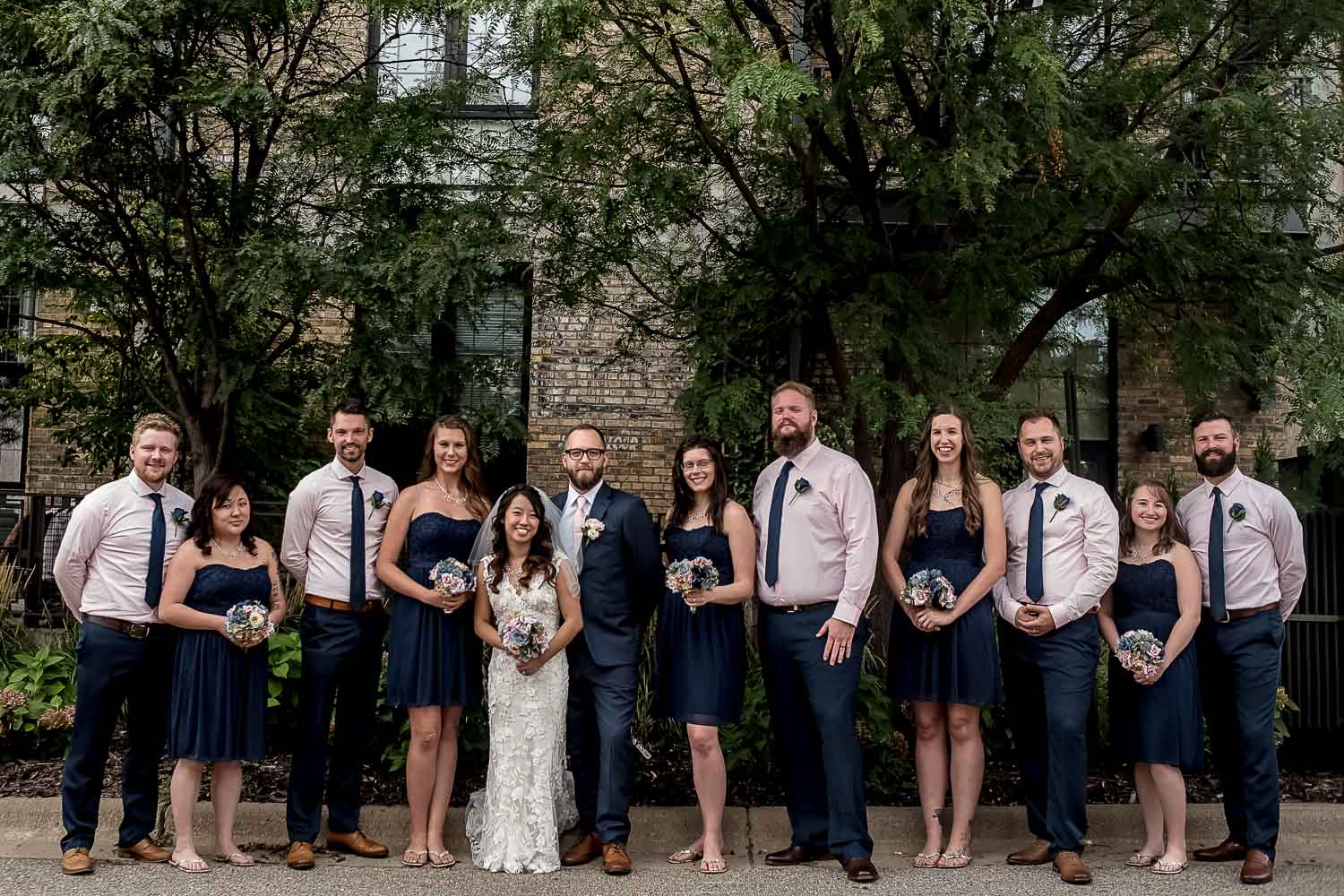 wedding party portrait with the bridesmaids wearing navy dresses and the groomsmen in pink shirts