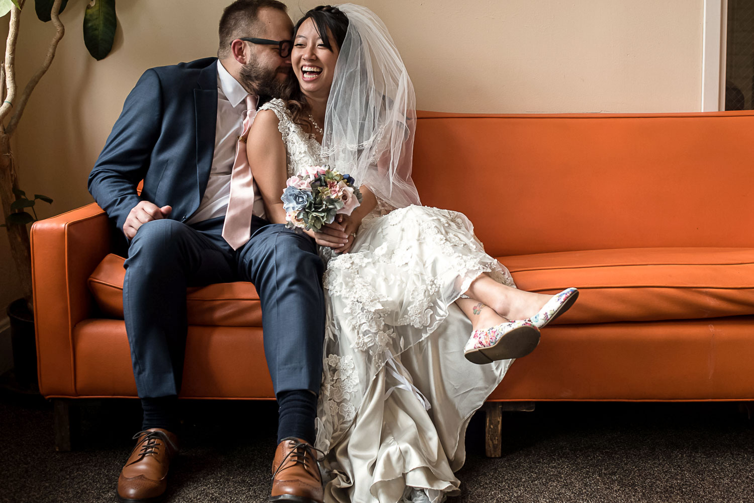 bride and groom snuggling on an orange sofa on their wedding day