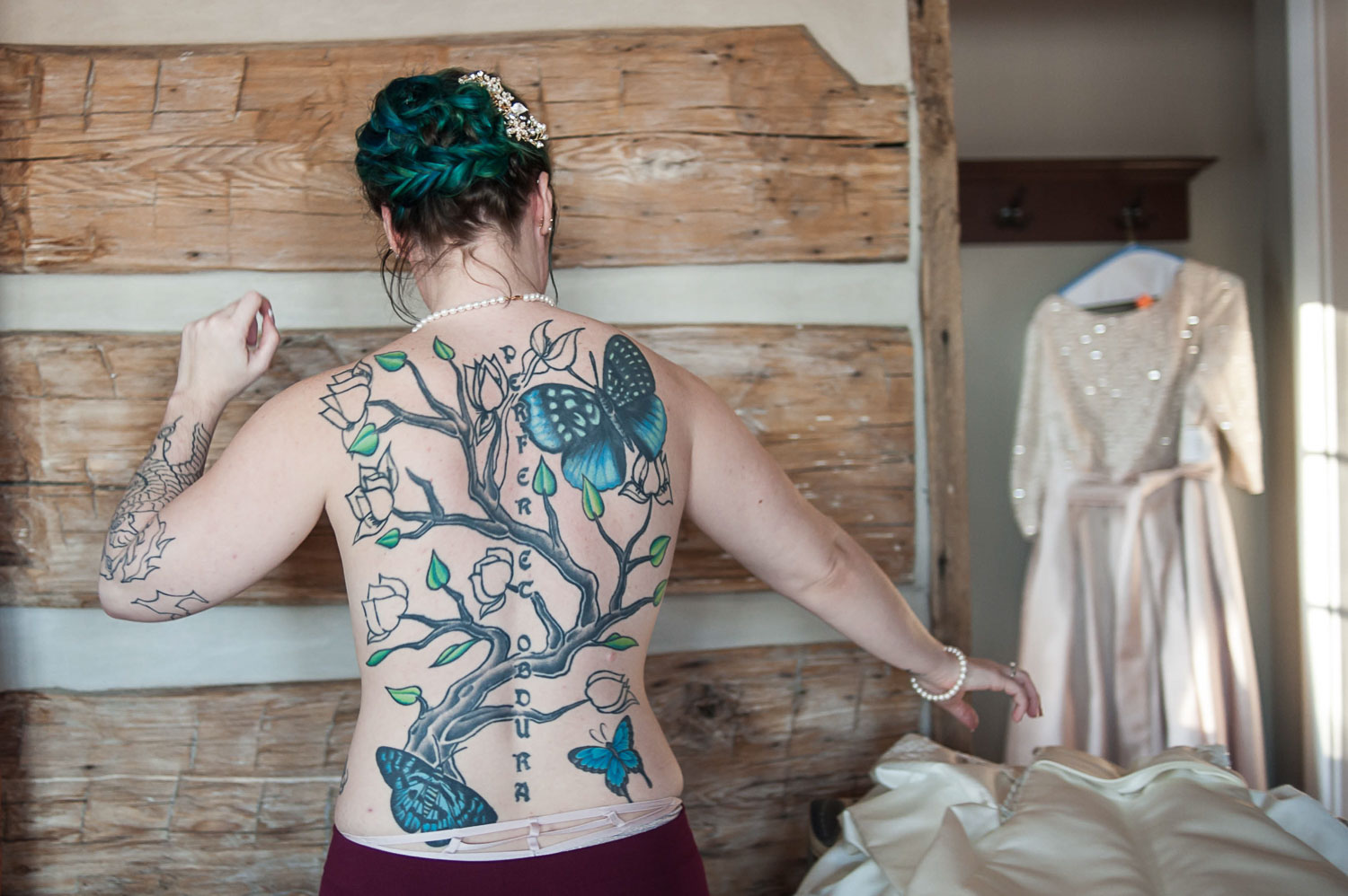 bride with a tattooed back getting ready to put her wedding dress on for her Minnesota wedding