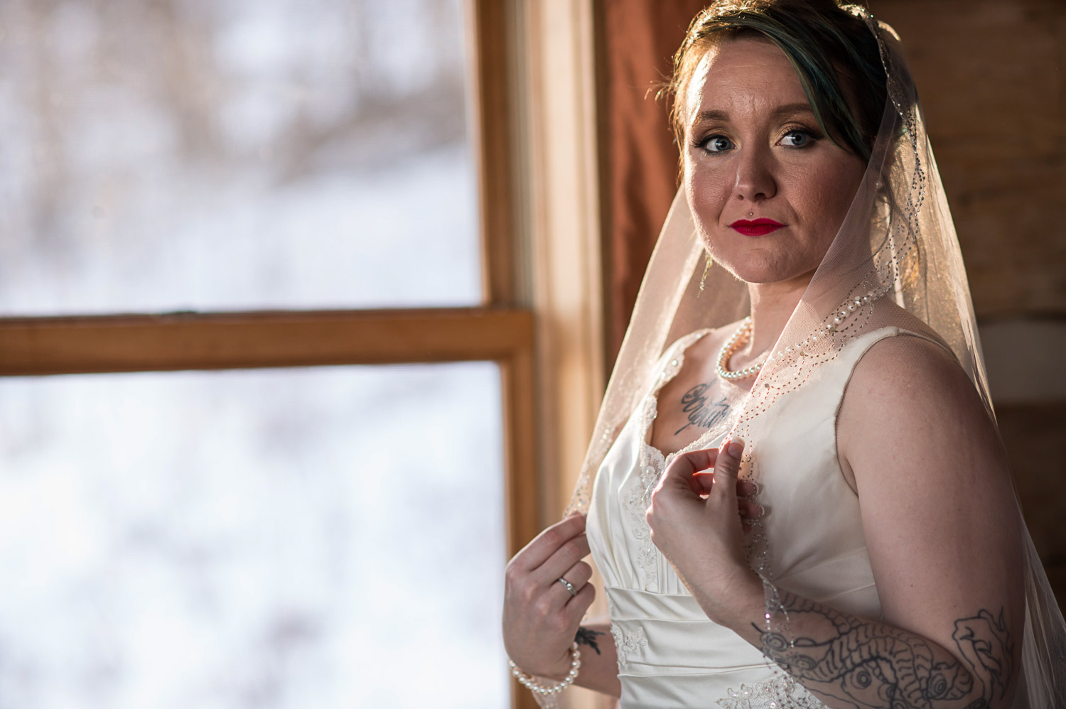 bride standing by the window holding her veil before her Minnesota winter wedding