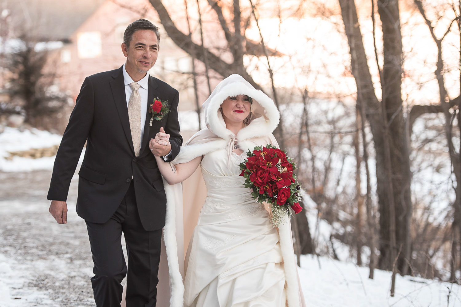 bride walking with her dad wearing a white fur lined cloak for her Minnesota winter wedding