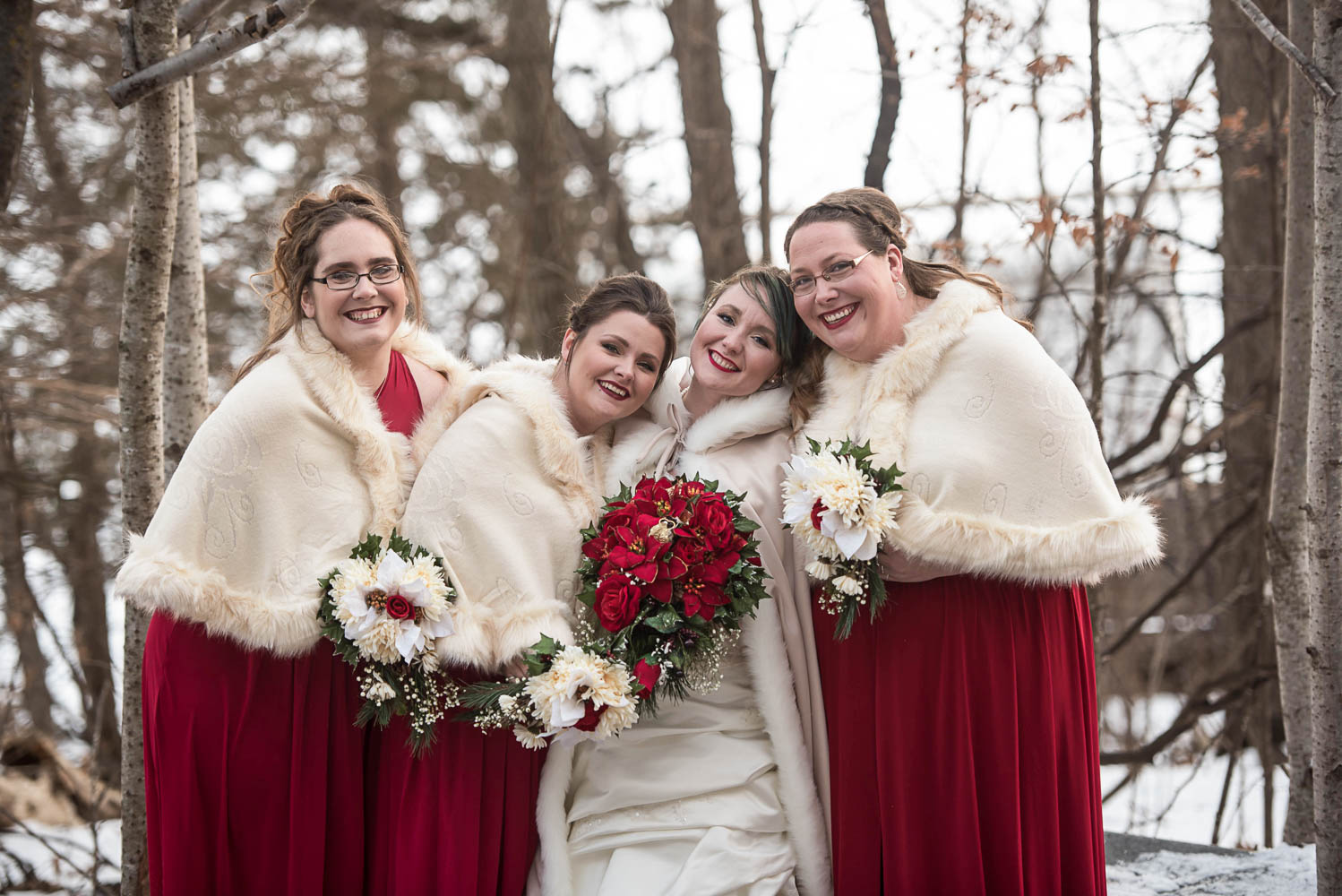 bridesmaids with the bride wearing white fur lined cloaks with red bouquets