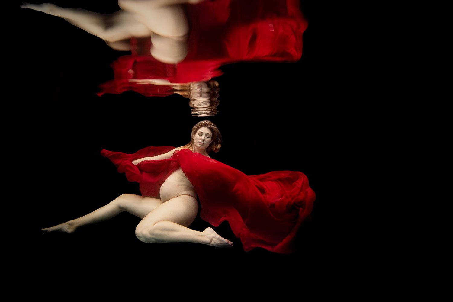 pregnant woman in a red cape doing a maternity session underwater