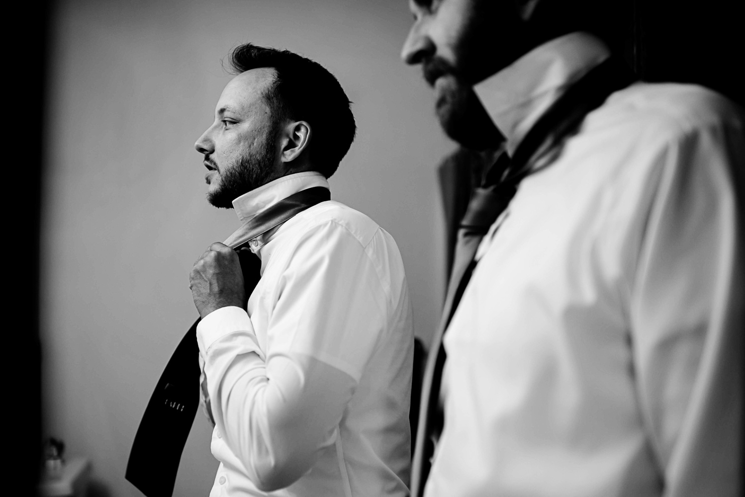 groom putting on his tie with his best man before the his wedding at home