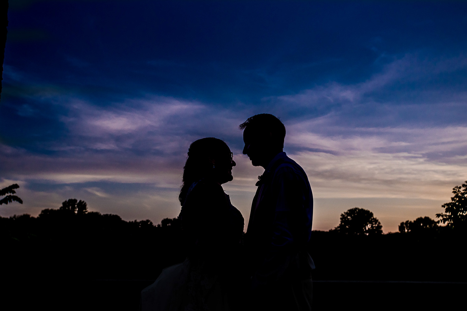 bride and groom's silhouette at sunset at their home at the end of their summer wedding 