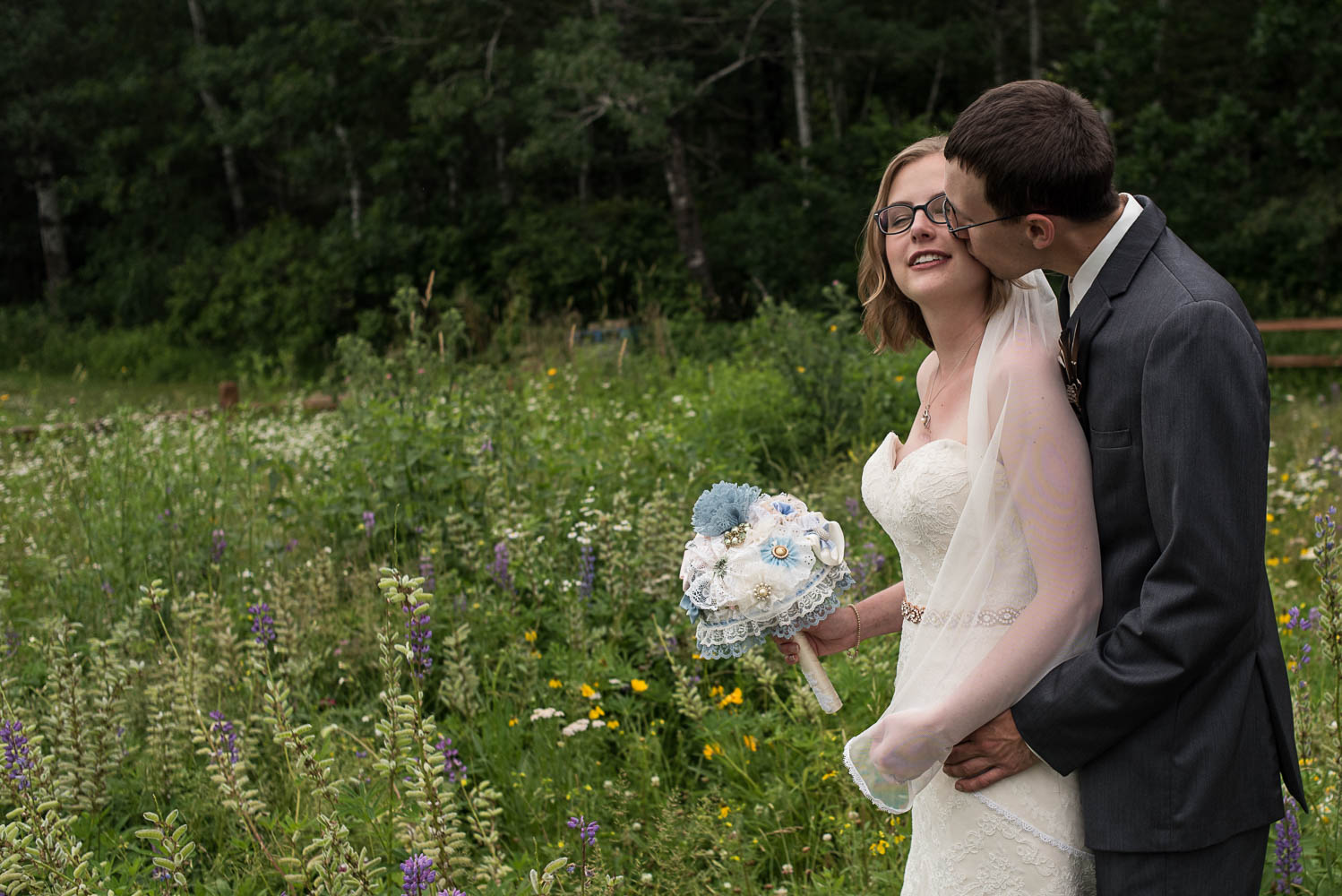 groom kissing bride on the cheek while standing in a field of flowers in Northern Minnesota