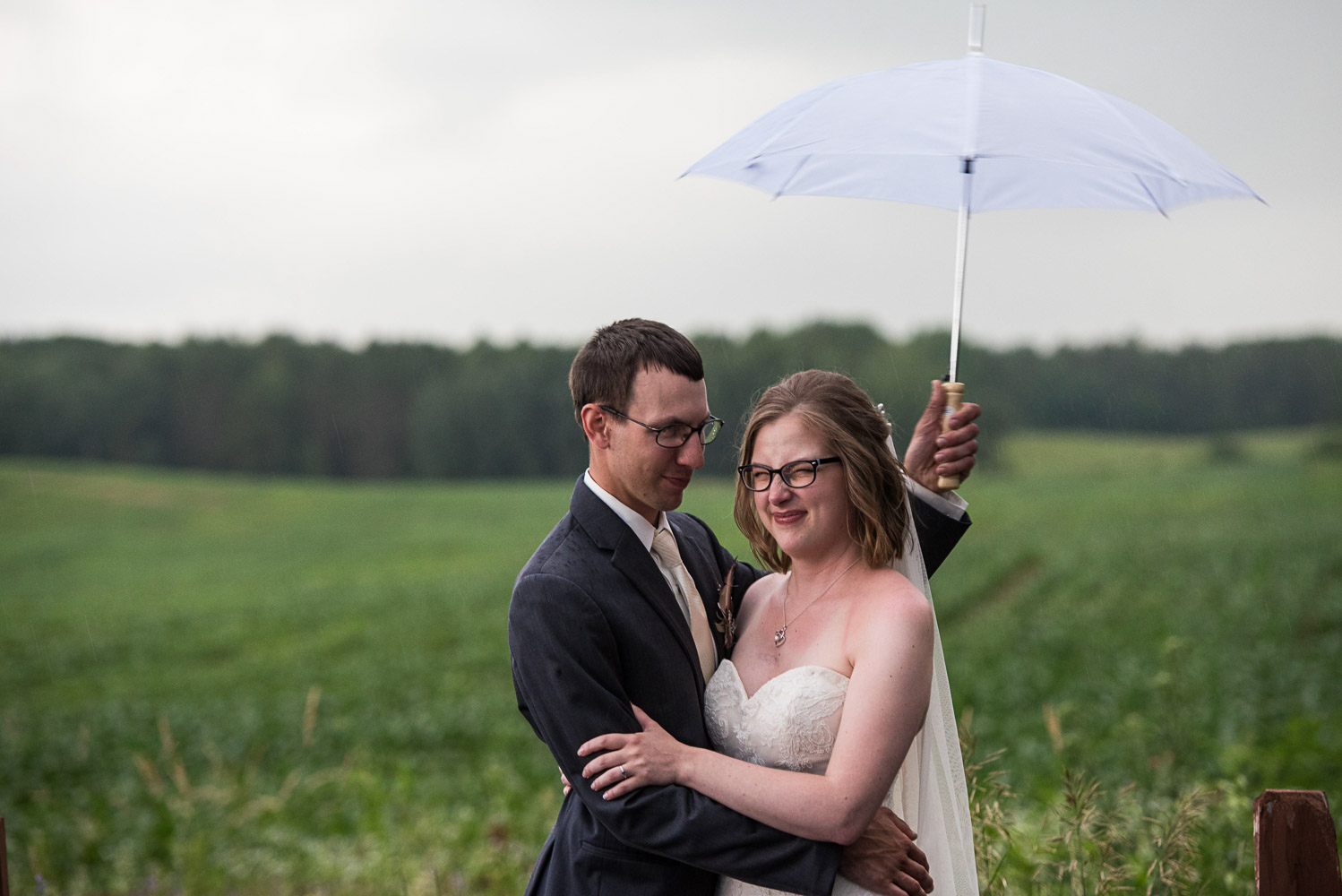 bride and groom holding a white umbrella in a field at Pine Peaks Wedding & Event Center