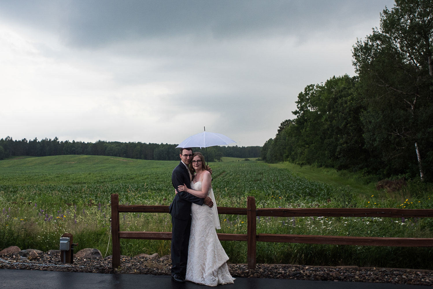 bride and groom hugging standing next to a fence and a field in Northern Minnesota at Pine Peaks Lodge