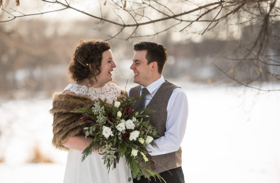 bride wearing a fur cape holding her winter bouquet laughing with the groom before their Minnesota winter wedding