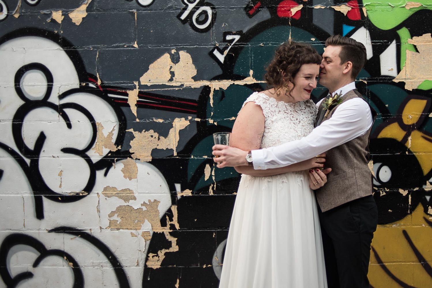 bride and groom hugging next to a graffiti wall behind Turtle's 1890 Social Centre before their winter wedding
