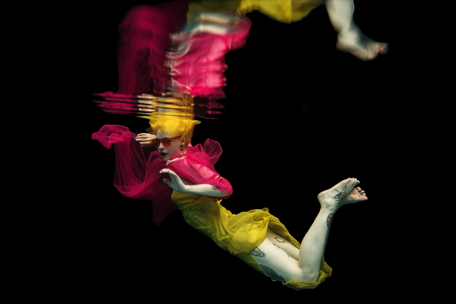 girl in a yellow dress with hot pink sunglasses and pink top with yellow hair in underwater