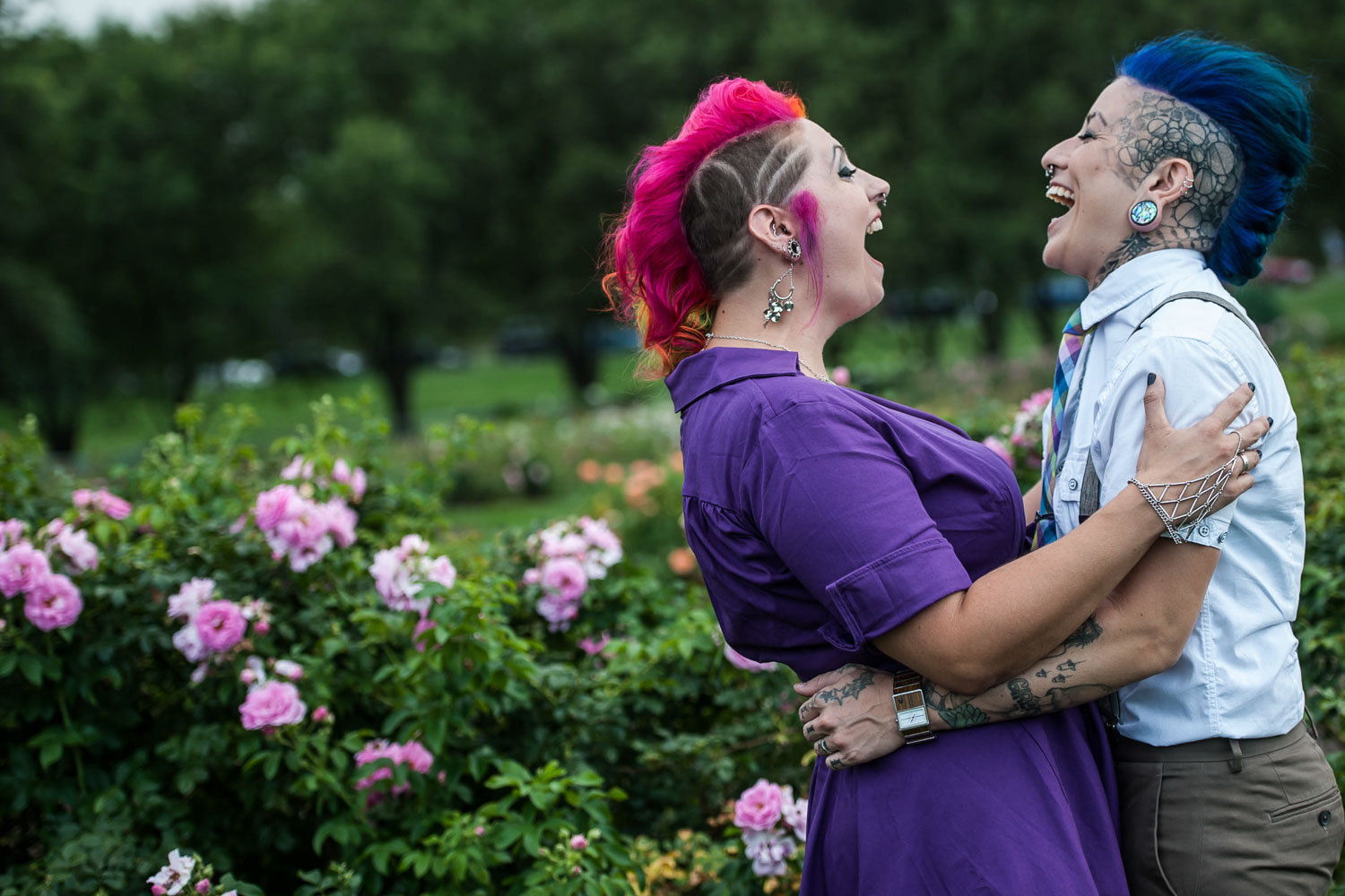 LGBTQ couple with pink and blue hair laughing during their engagement session
