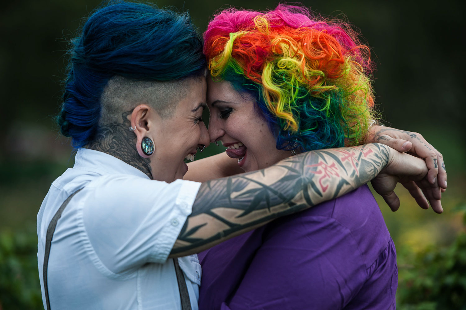 LGBTQ couple with rainbow hair touching foreheads and laughing during their engagement session