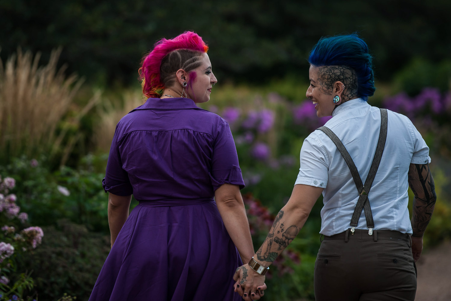lesbian couple holding hands looking at each other holding hands walking through a rose garden