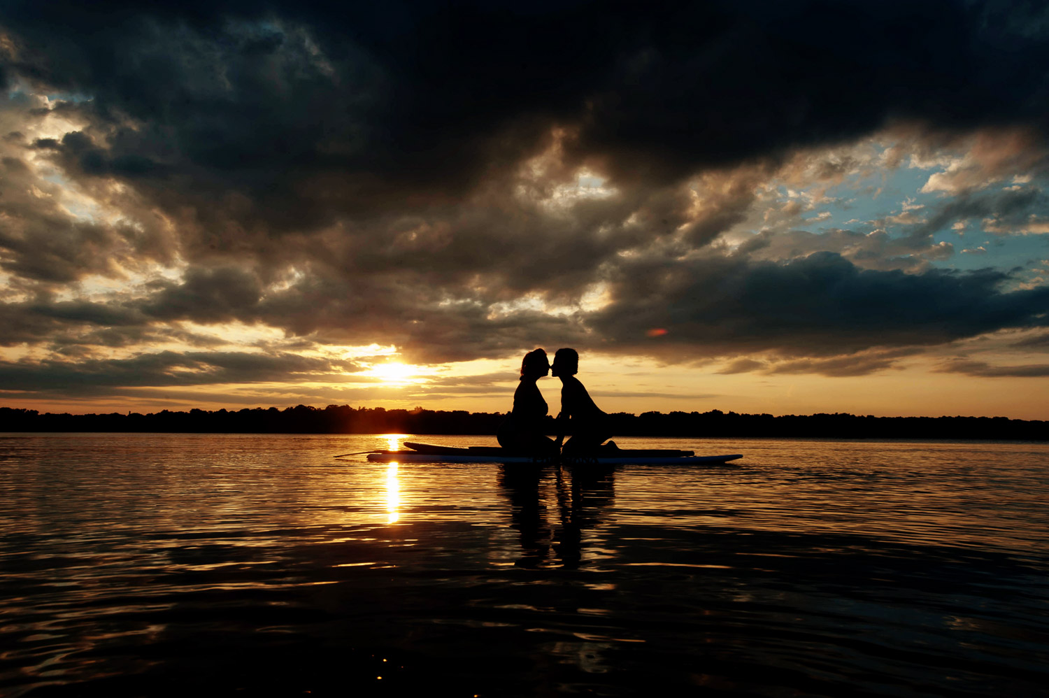 same sex couple kneeling on a paddleboard kissing on Lake Harriet