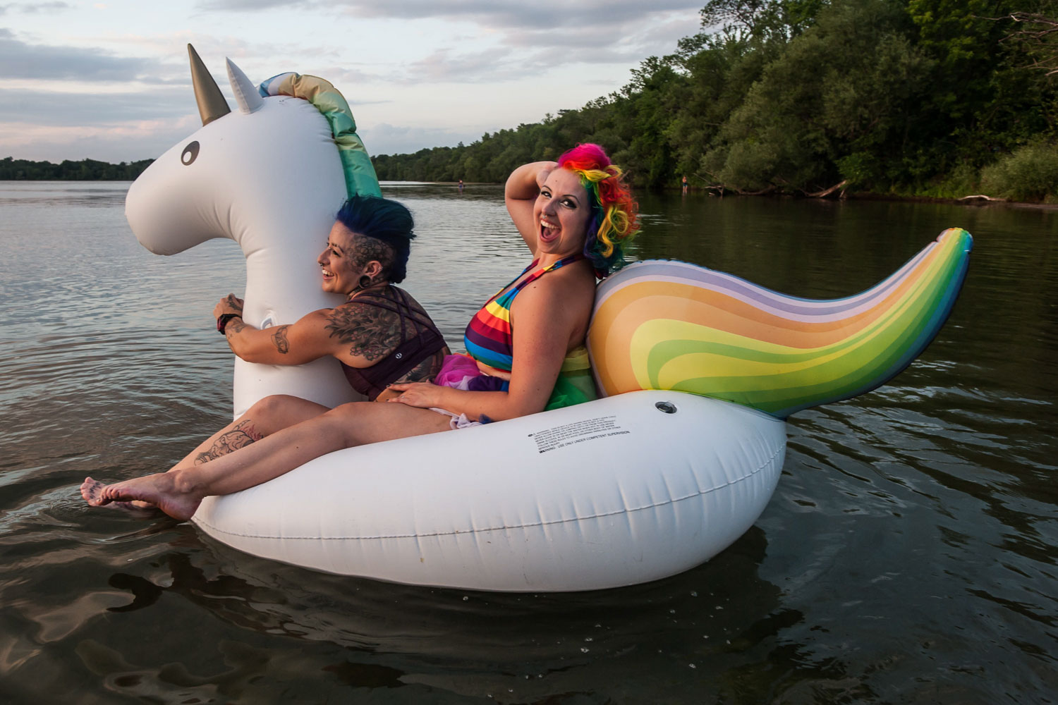 LGBTQ couple wearing rainbow swimming suits riding a rainbow unicorn