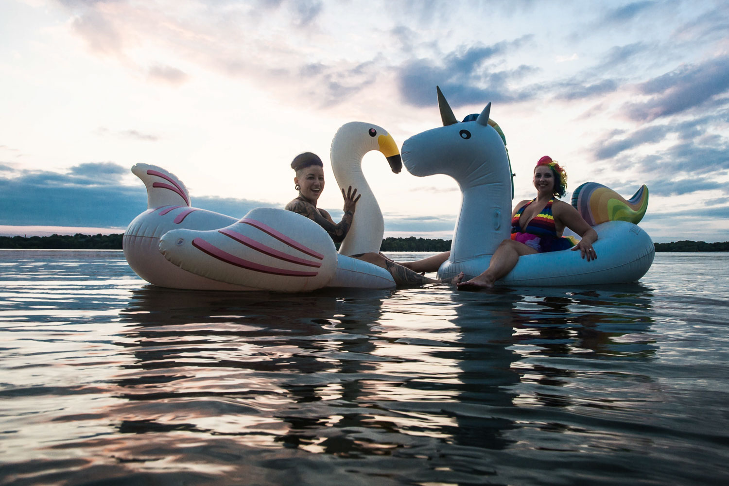 same sex couple riding a unicorn and flamingo pool floats