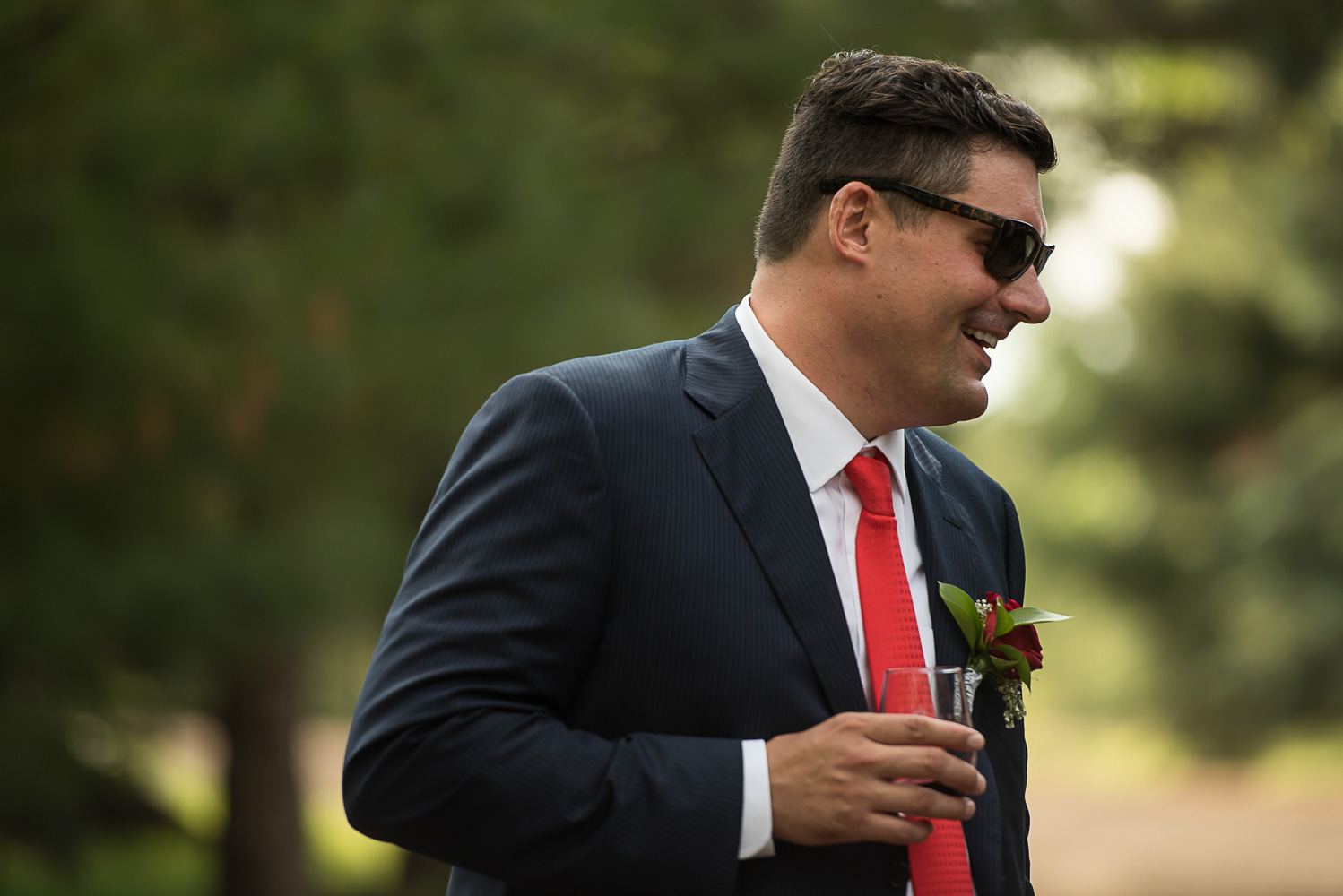 groom with a blue suit and red tie wearing sunglasses and holding a martini at the Winery at Sovereign Estate