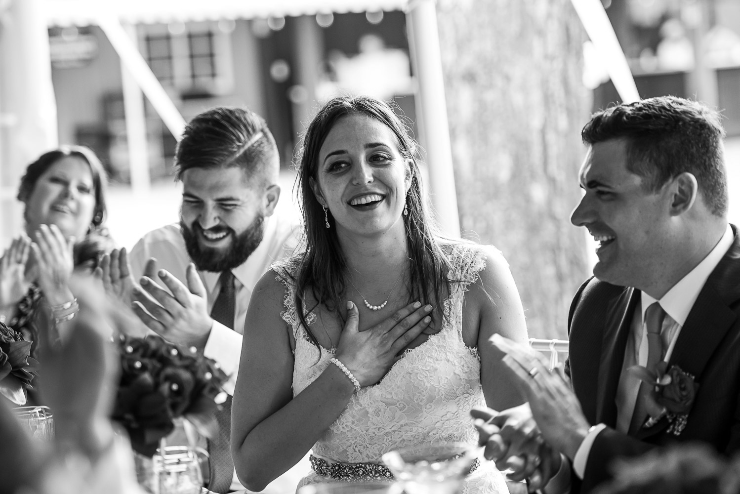 bride and groom sitting at the head table with the wedding party laughing while listening to speeches atthe Winery at Sovereign Estate