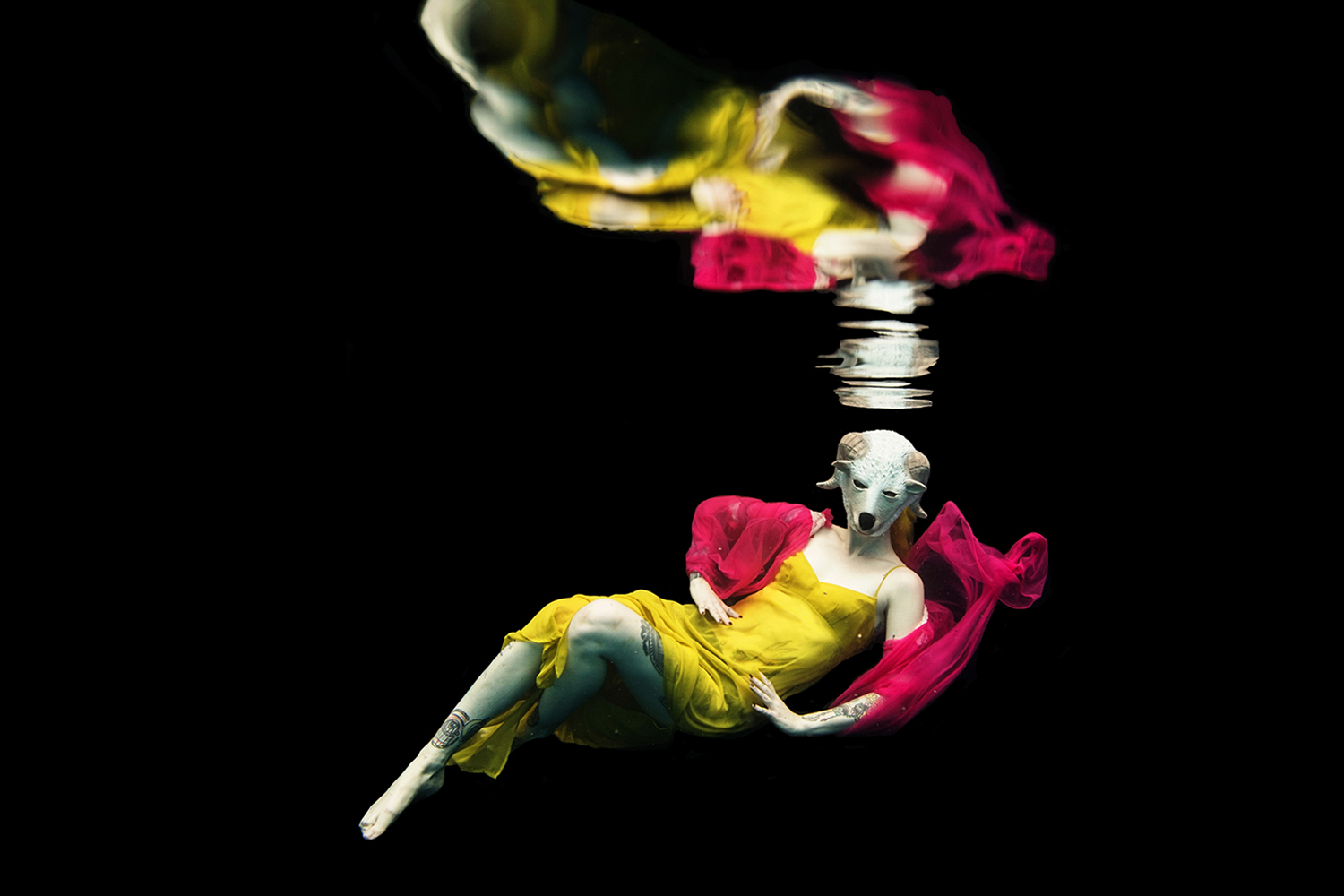woman wearing a yellow dress and a hot pink shirt wearing a sheep mask underwater