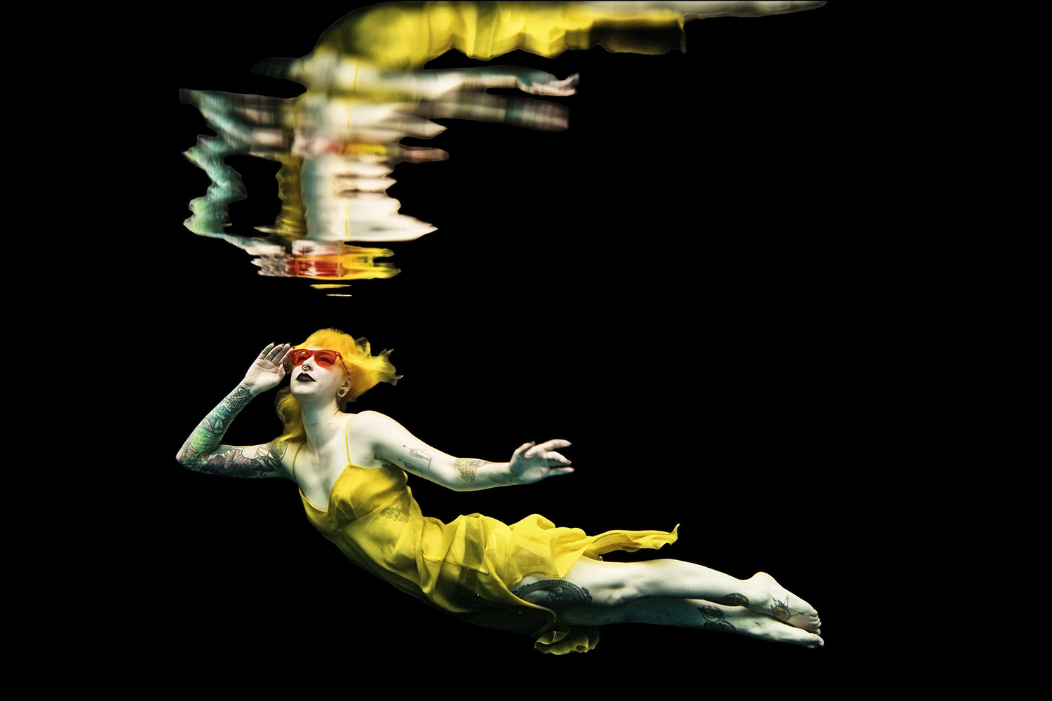 woman with yellow hair wearing a yellow dress with hot pink sunglasses underwater