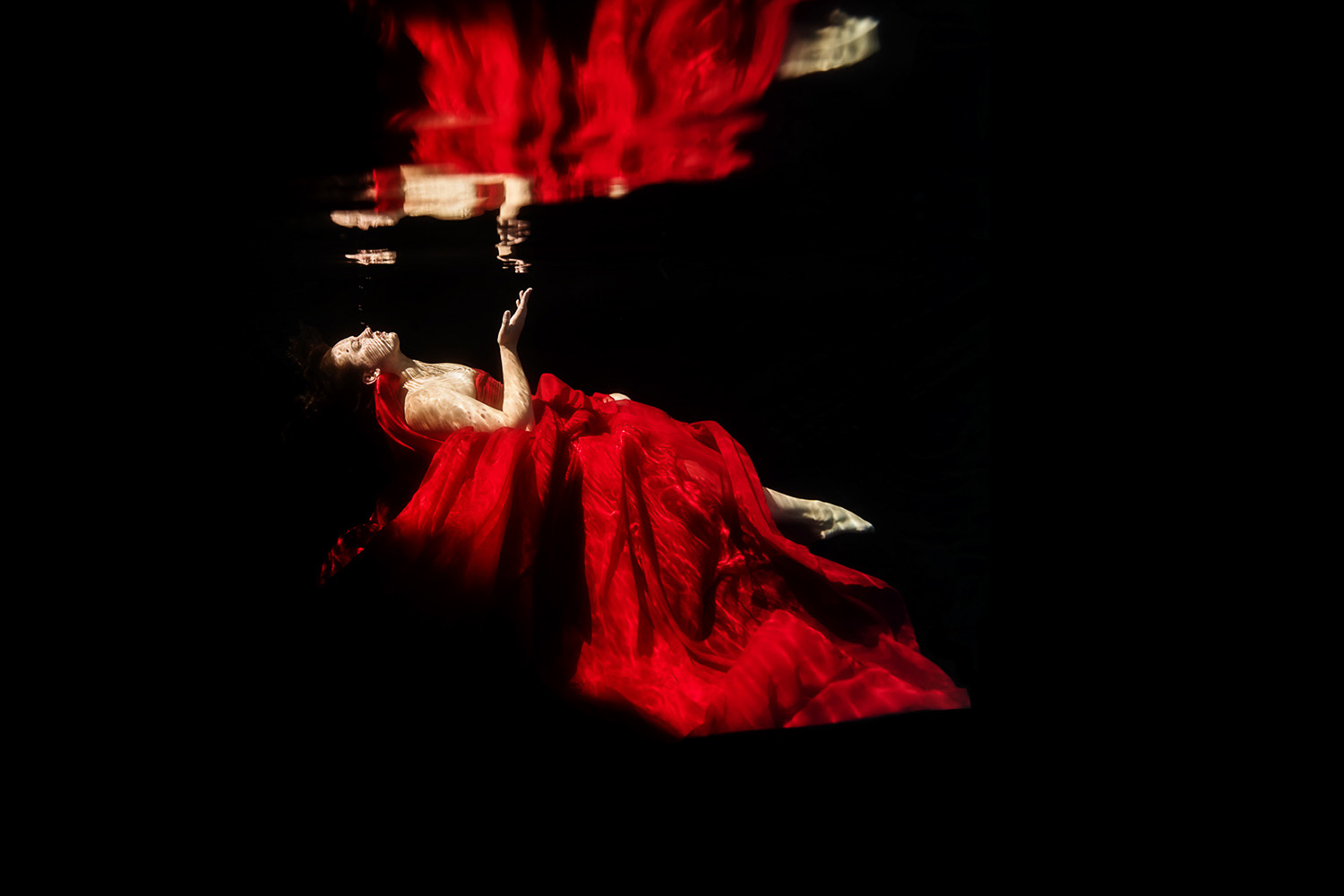 woman in red underwater refected on the surface of the water