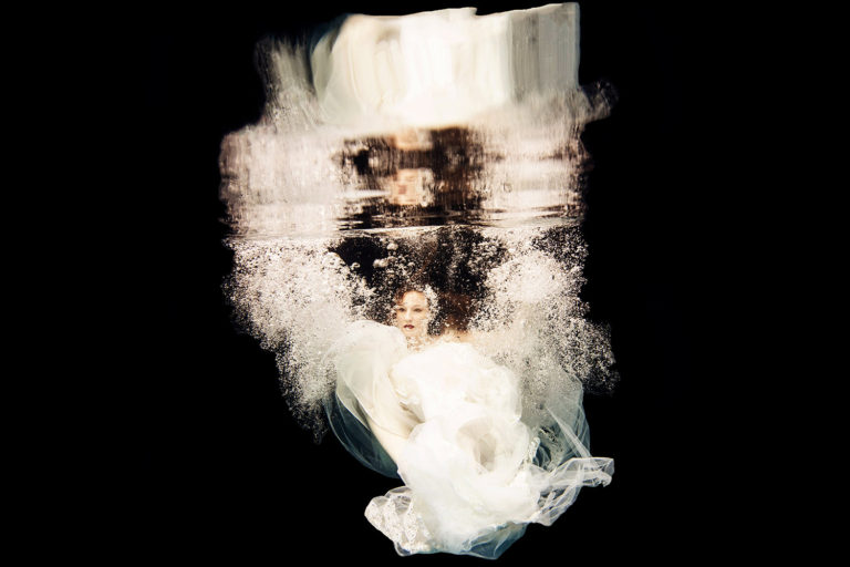 woman underwater wearing a white wedding dress surrounded by bubbles