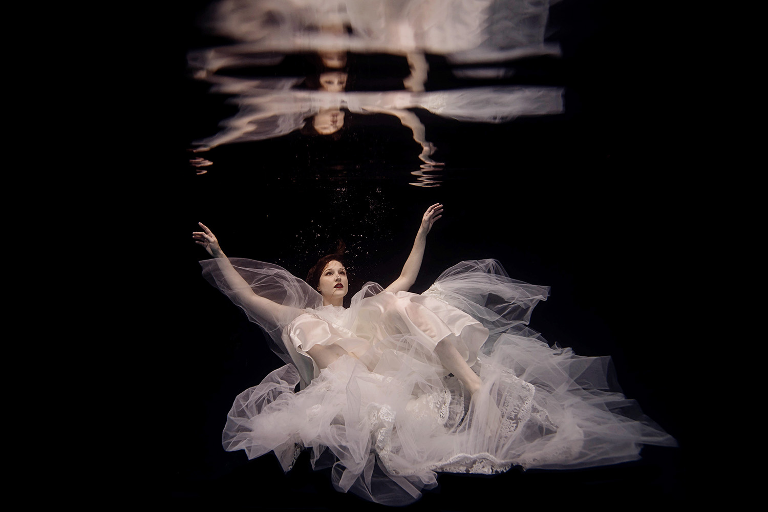 woman laying back with her arms in the ar=ir surrounded by a white lace wedding dress
