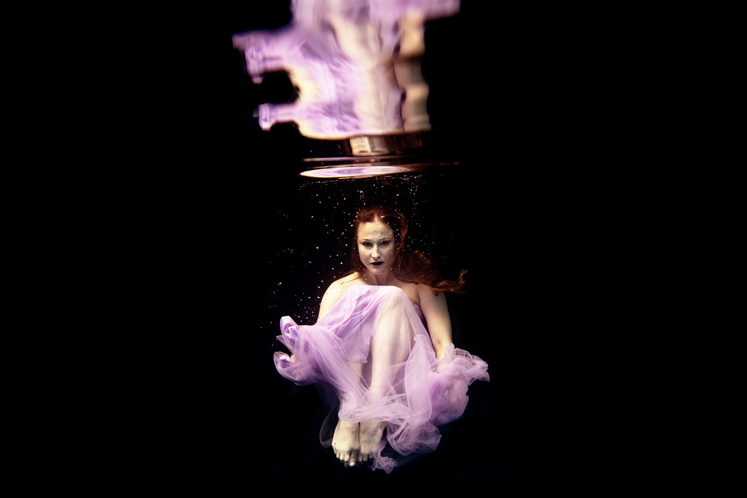 woman in a purple dress sitting underwater refected at the top