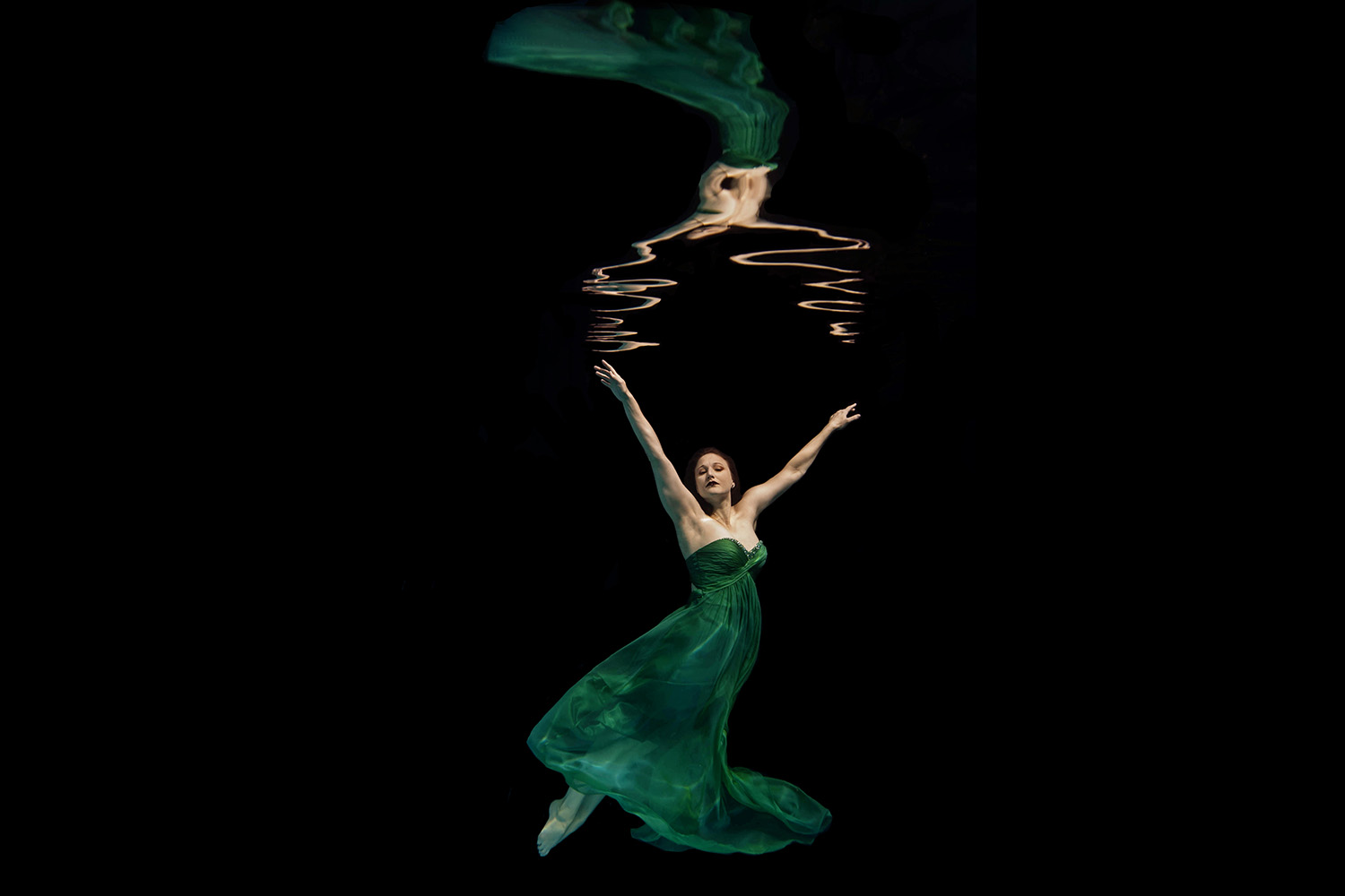 woman in a green dress underwater with her warms in the air and toes pointed