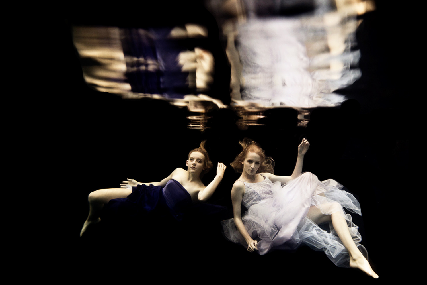 two women underwater wearing a purple dress and a white dress