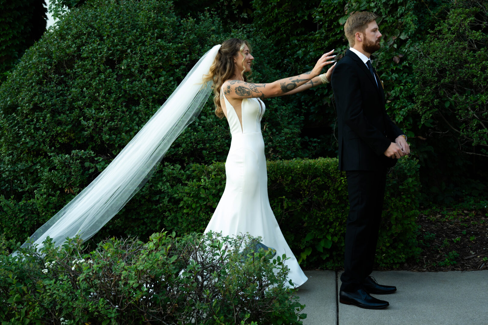 Bride stands behind groom with arms outstretched and on his shoulders moments before he turns around for the first look wedding picture.
