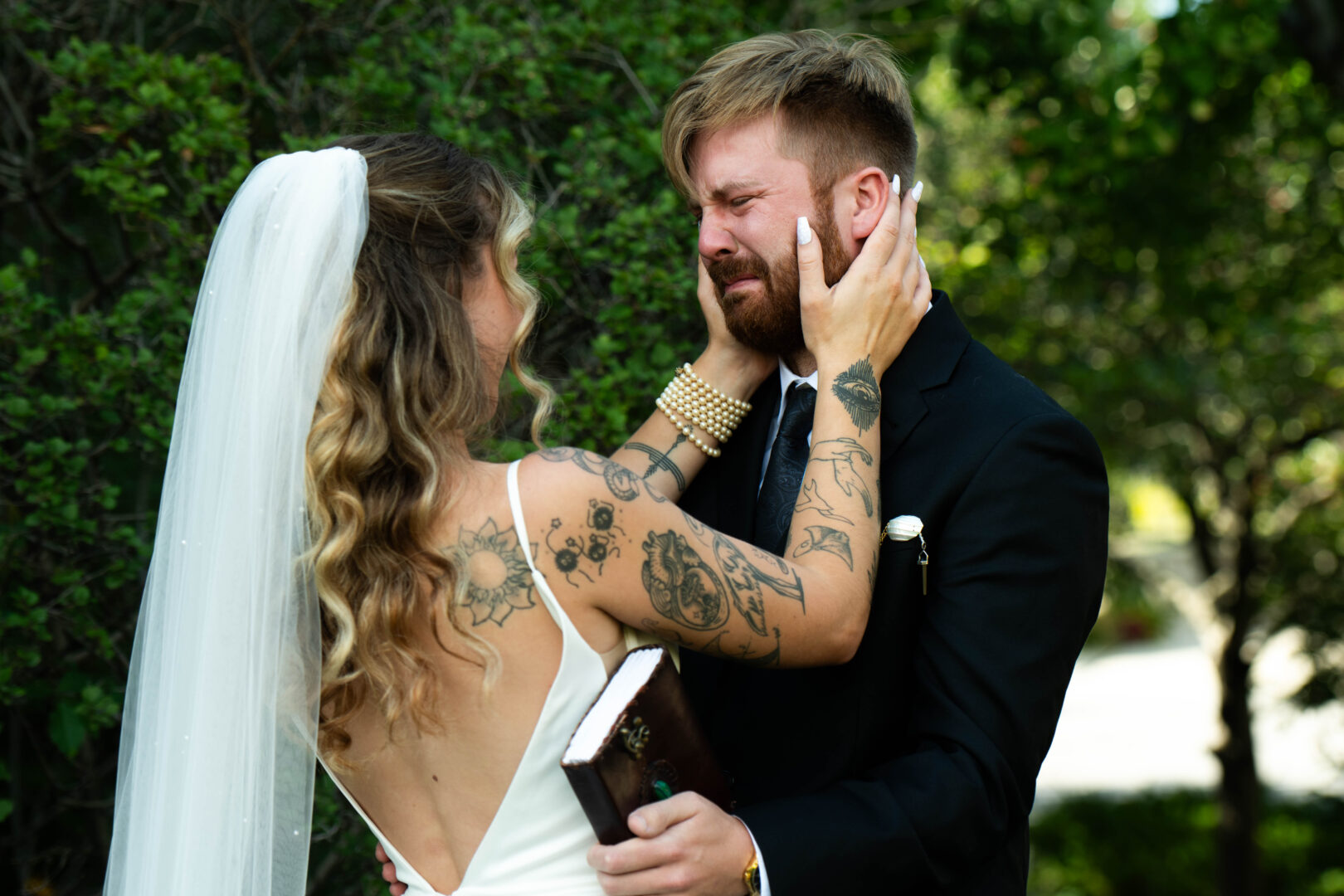 Bride caresses grooms face as he cries during first look.