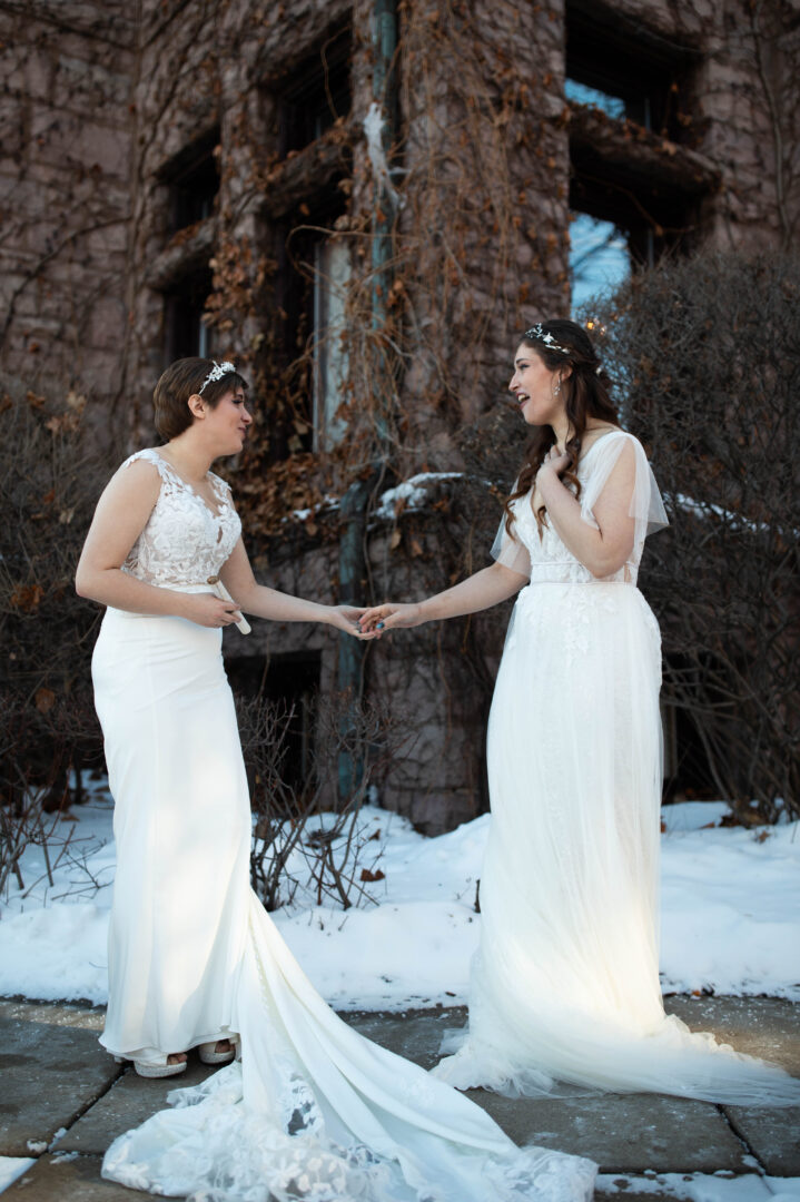 Brides hold hands as they see each other in their wedding gowns for the first time prior to wedding ceremony.