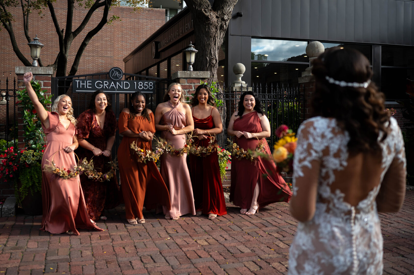 Bridal parts dressed in various shades of red cheer as they see bride in her wedding gown for the first time prior to wedding ceremony.