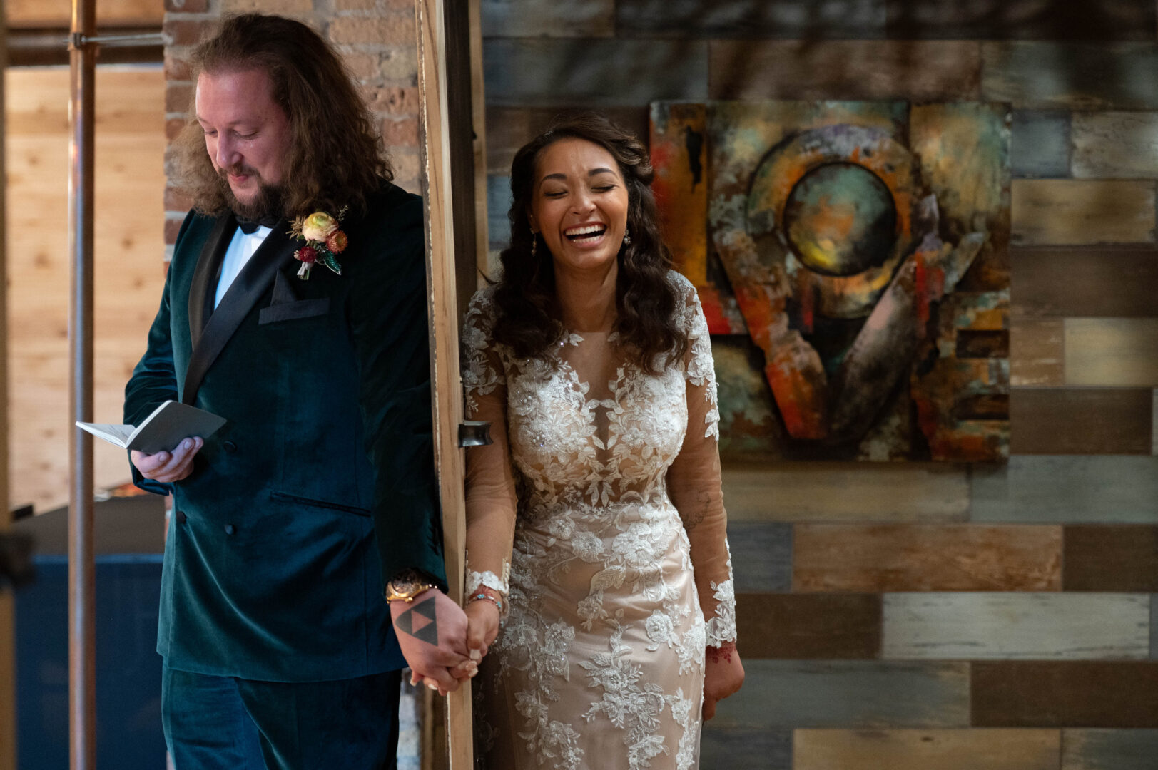 Bride and groom hold hands as they stand on separate sides of wall moments before first look prior to wedding ceremony.