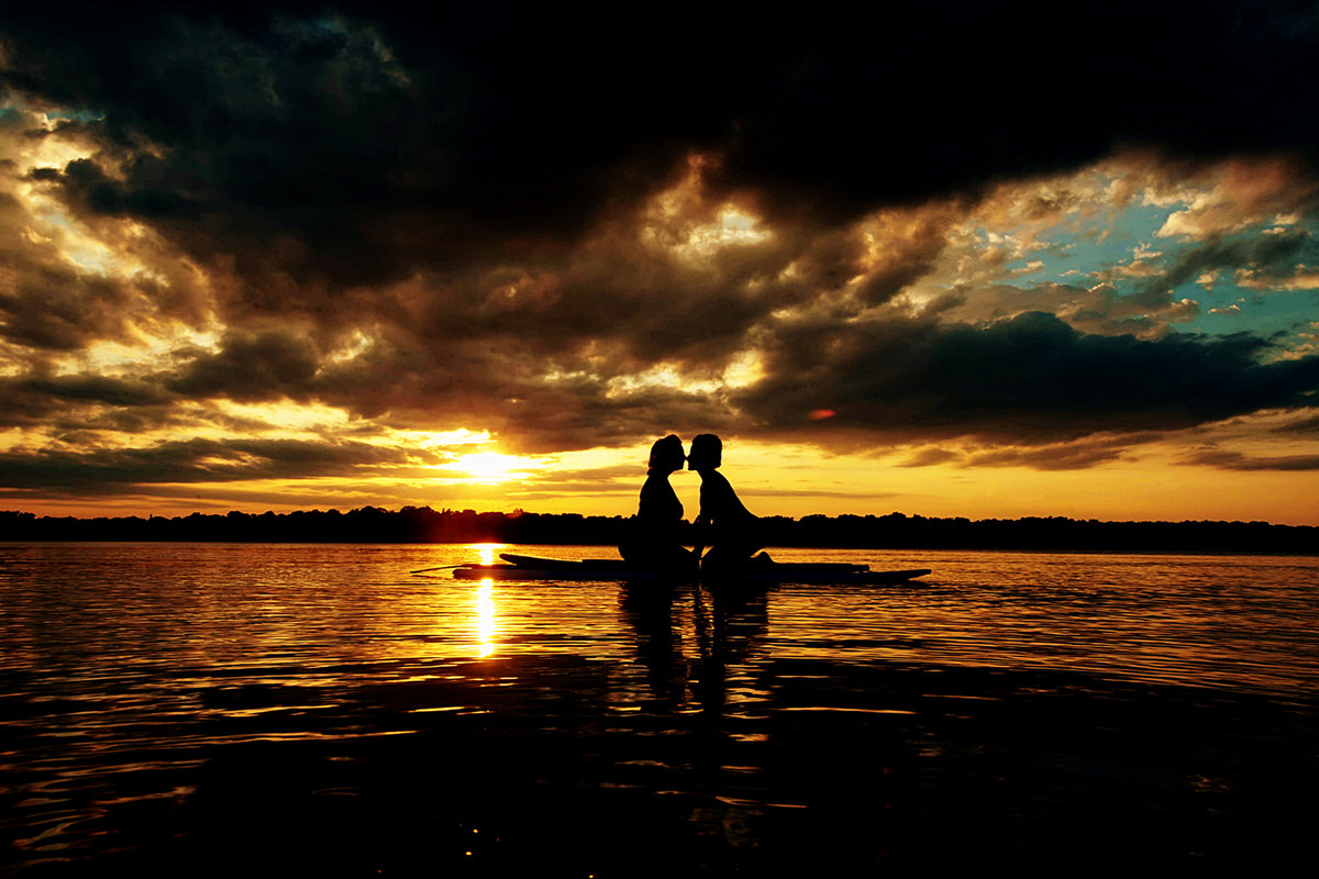 The silhouette of a couple about to kiss while kneeling on a paddle board