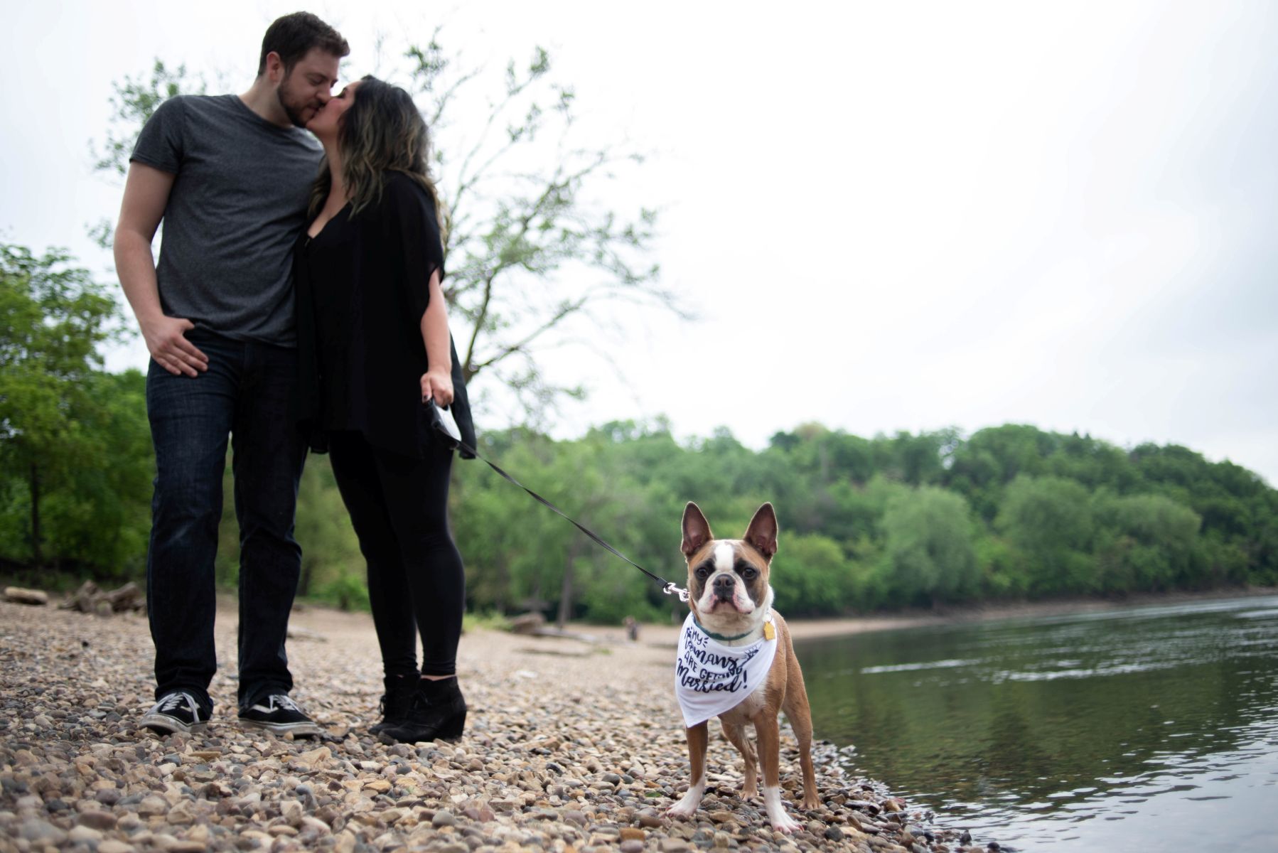a couple standing next to the water at hidden falls taking engagement photos and holding their dog's leash