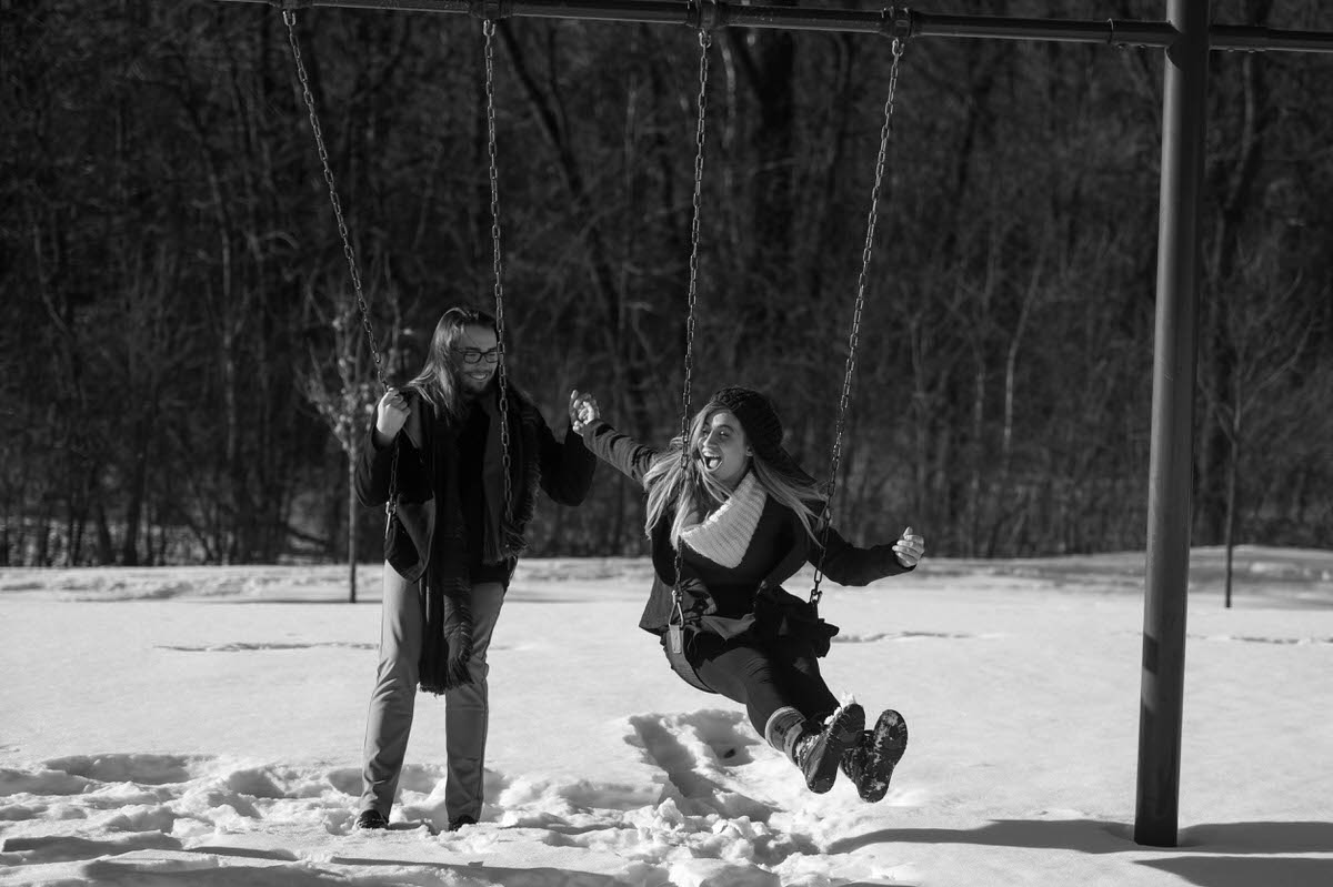 a couple taking engagement photos on a swingset in the snow